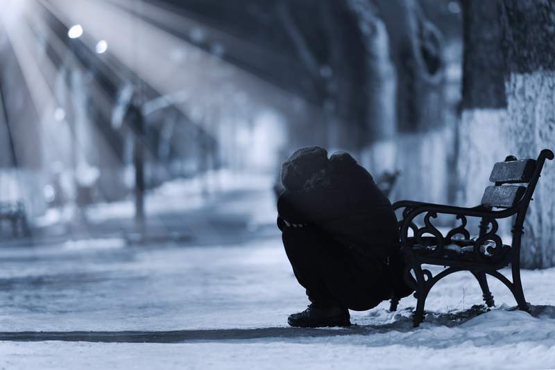 Depressed woman sitting on the ground in front of a park bench