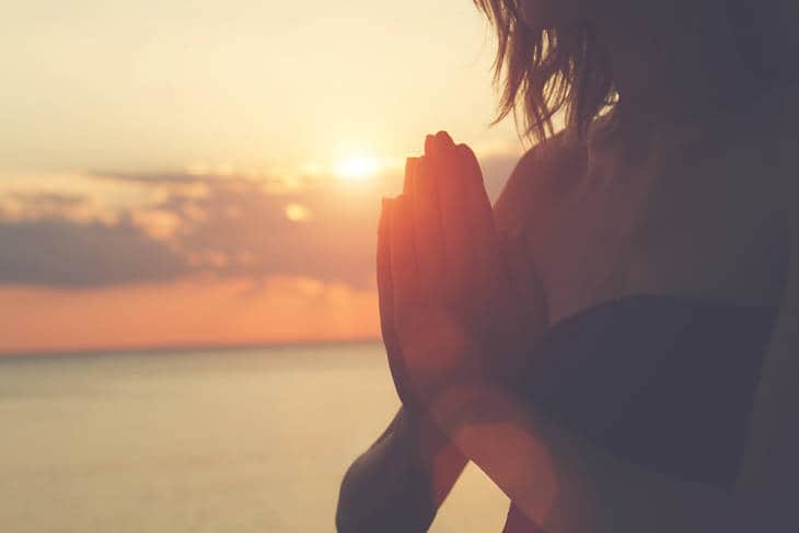 Woman praying at sunrise on beach
