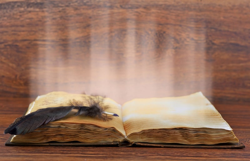 Old book with quill and light flowing out of it