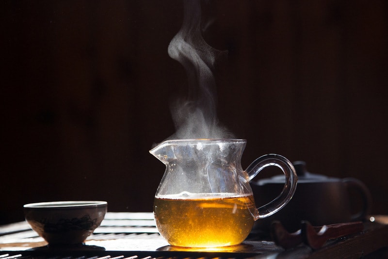 porcelain cup with glass jug of steaming tea