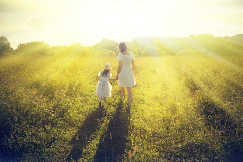 mother and daughter walking in sunlit meadow