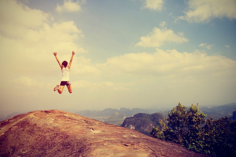 Young Asian woman jumping for joy on top of mountain