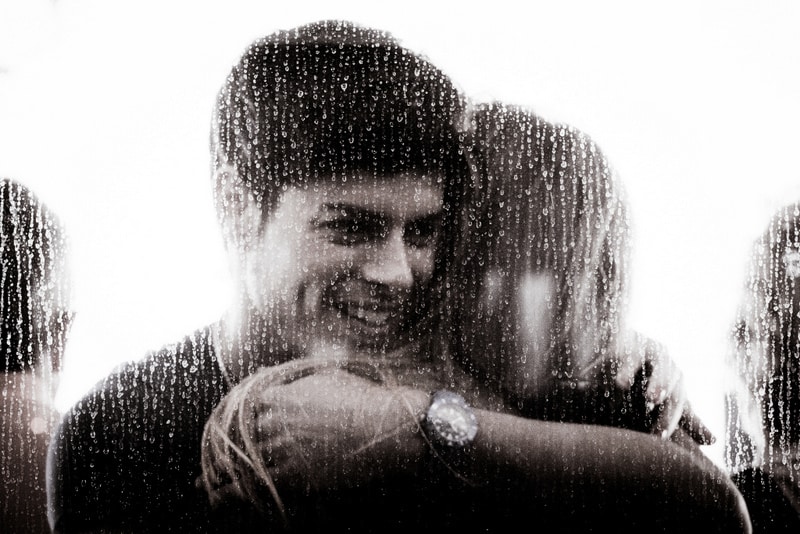 Man and woman hugging on the other side of a rain-dropped window
