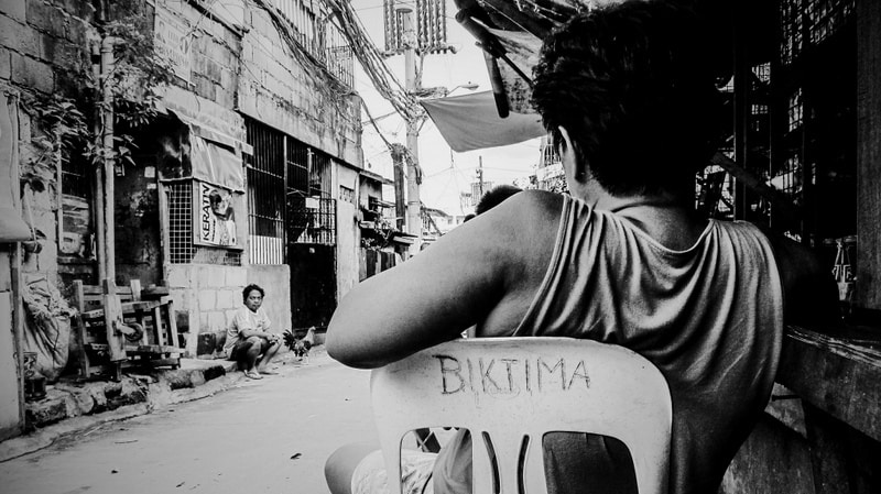 Woman sitting on a chair with the word 'victim' on the back written in Tagalog