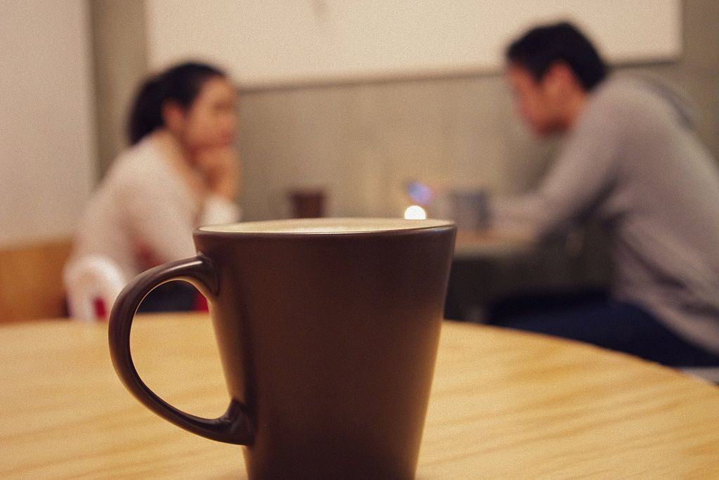 A young man and woman have a quiet conversation with a coffee cup in the foreground - Myers-Briggs humour