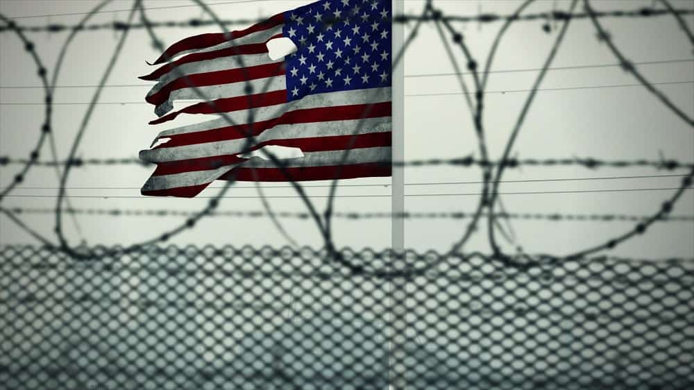 American flag with holes hanging on jail fence - The True American