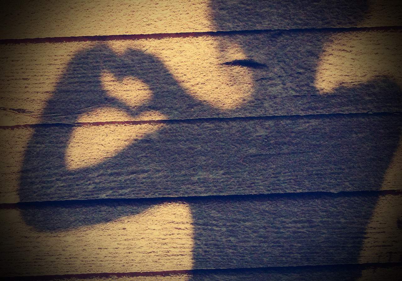 Girl making shadow of heart with hands on wooden wall - Living with intention