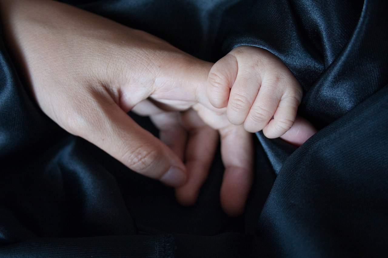 Mother holding baby's hand on top of blanket - Love warrior