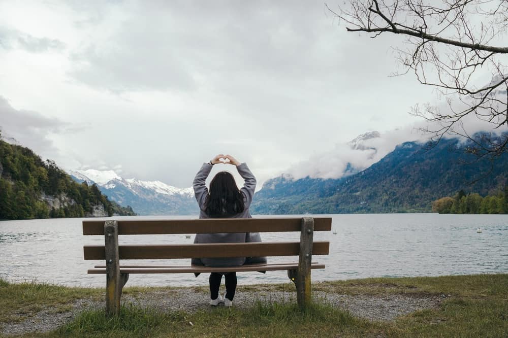 FROM ANXIETY TO LOVE: Disconnect from your ego and connect with your Inner Therapist 13 Woman sitting on bench in front of water, stretching arms overhead, making heart with hands - From anxiety to love