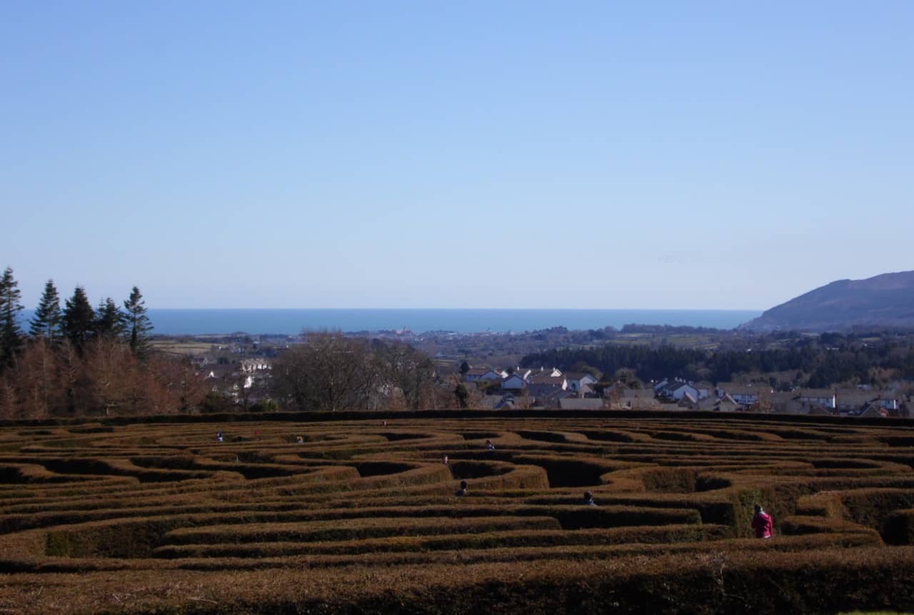 People walking through garden maze with houses in background - Poems by Colin James