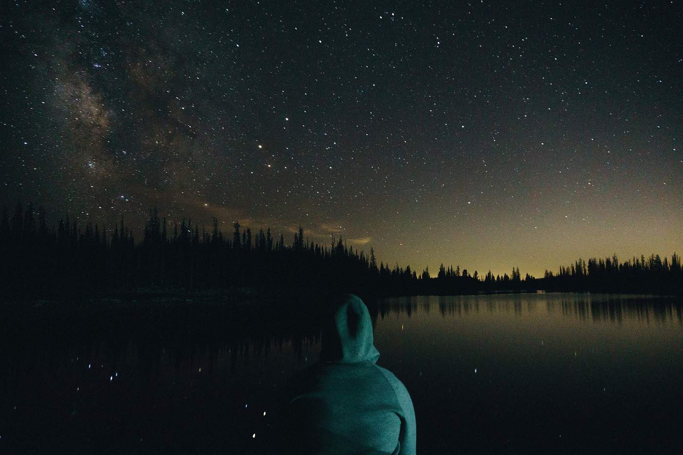 Hooded person thinking in front of starry sky and water - War trauma therapy