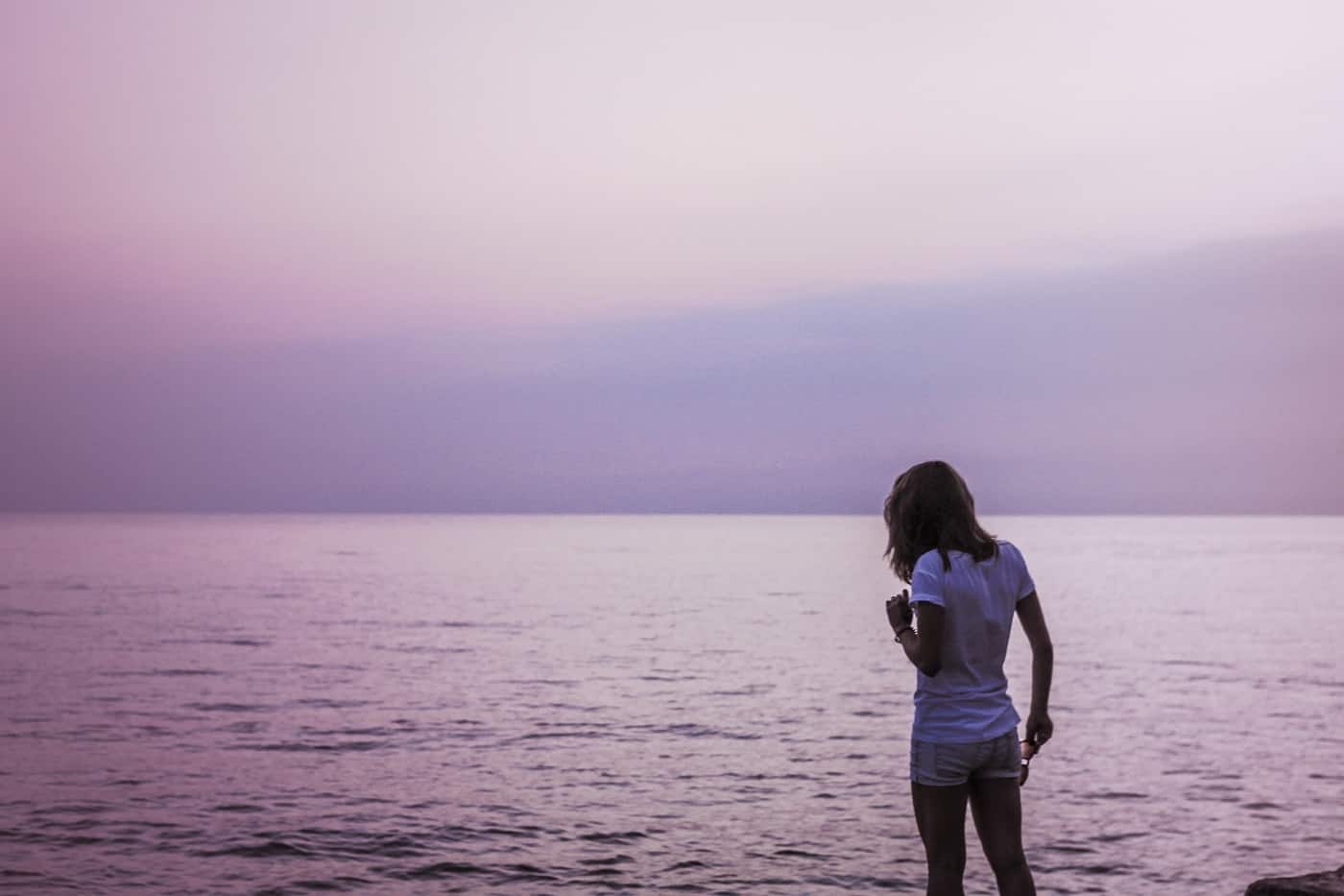 Purple-tinged image of woman standing next to body of water