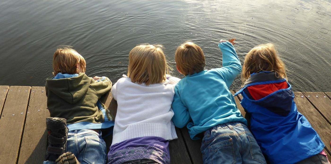 children lying on a dock throwing stones into the water