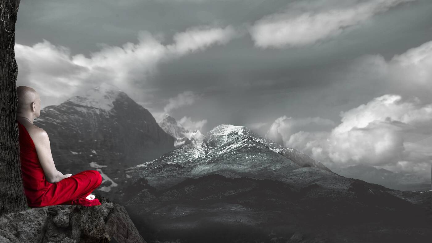 Buddhist monk with red robe sitting beside mountains