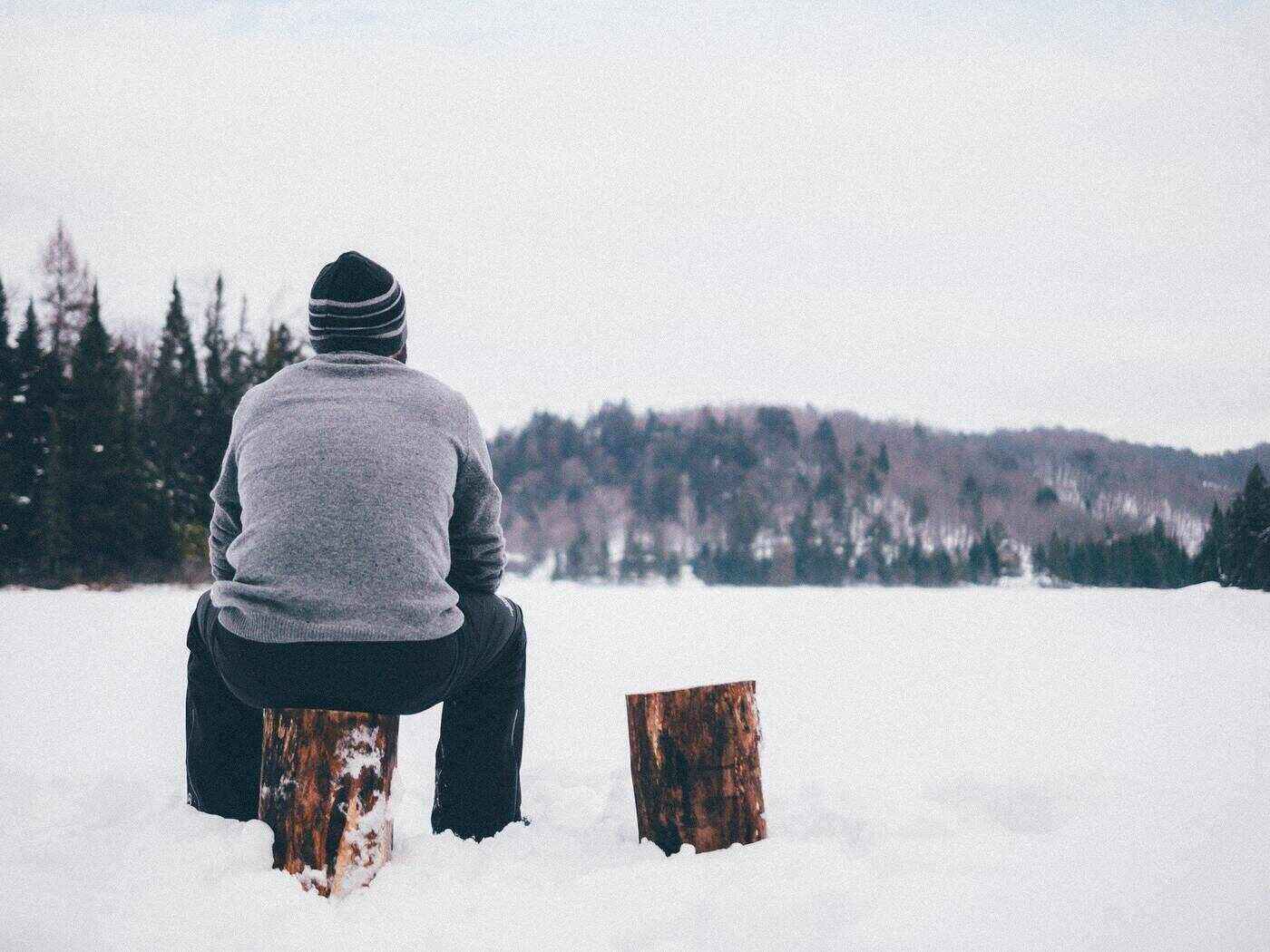 Man sitting on piece of log in snow