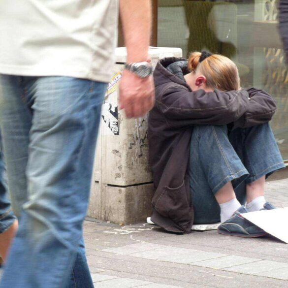 Homeless woman sitting on street as people walk by