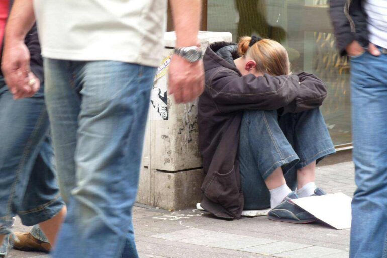 Homeless woman sitting on street as people walk by