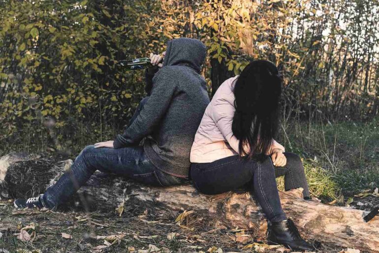 Two friends sitting back to back, one drinking from alcohol bottle