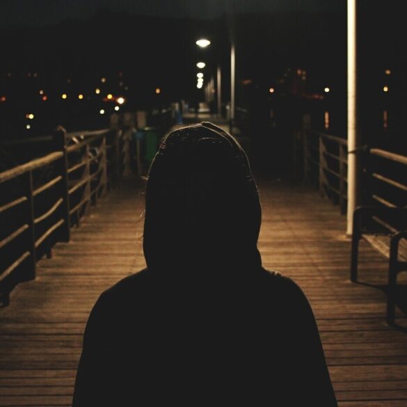 Lone person walking across bridge in dark, wearing hoodie