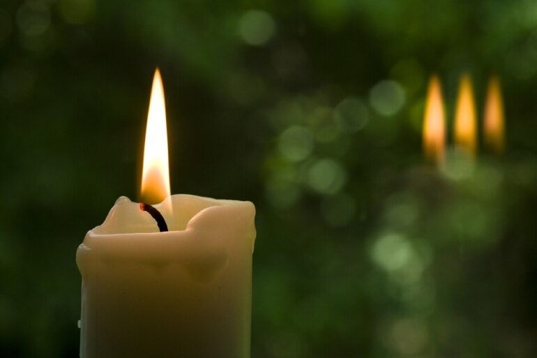 White candle against background of green plants