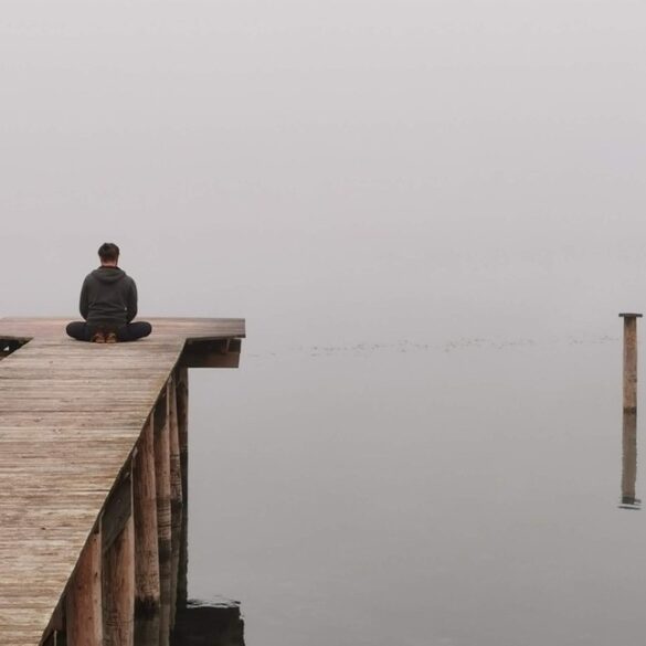 Man meditating on dock by lake