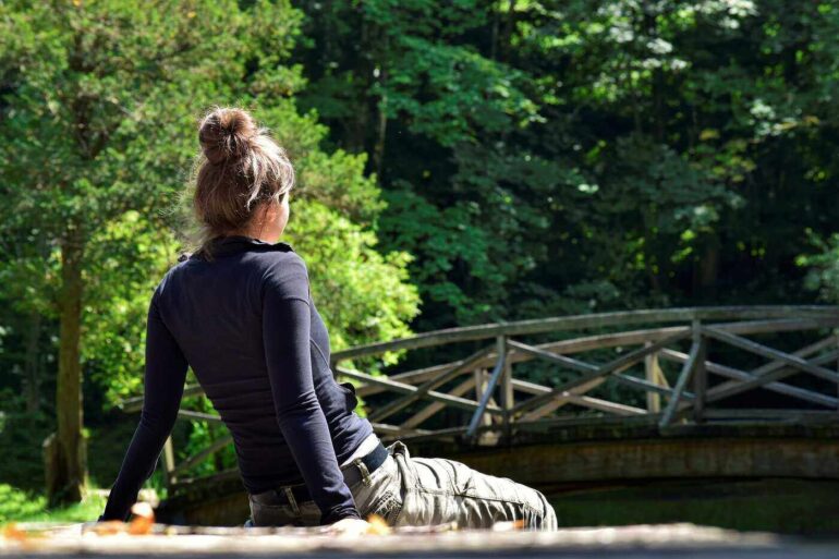 Young woman sitting on dock in front of bridge