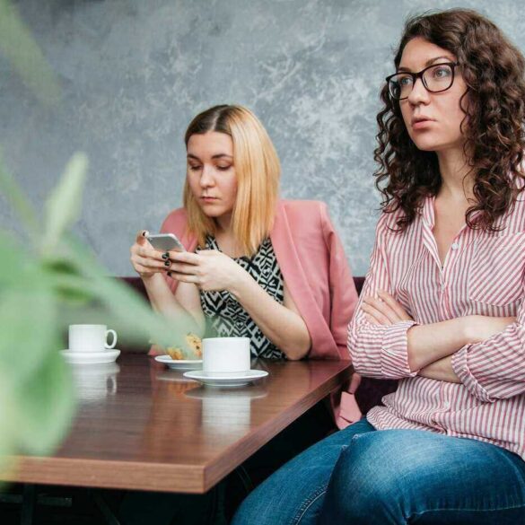 Two grouchy young women having coffee at table
