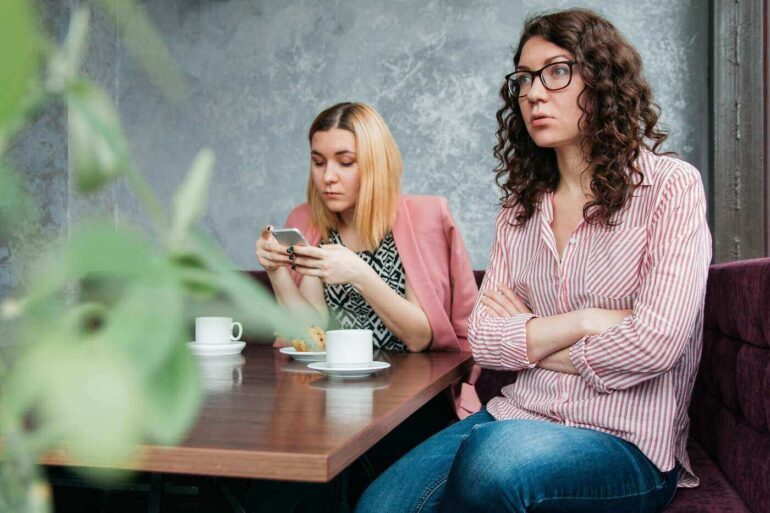 Two grouchy young women having coffee at table