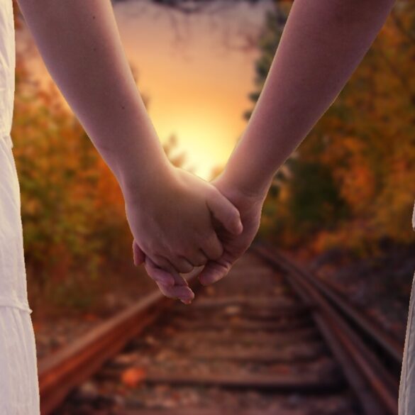 Couple holding hands, walking towards sun on train track