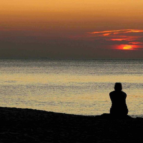 Person sitting quietly on beach at sunset