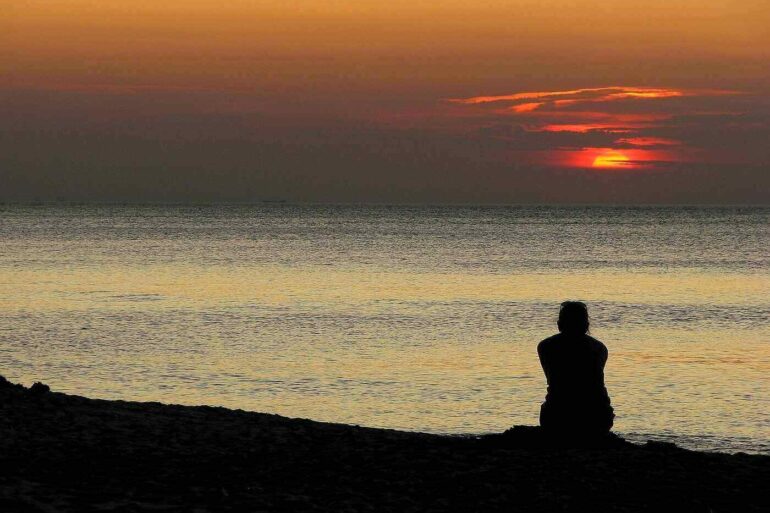 Person sitting quietly on beach at sunset