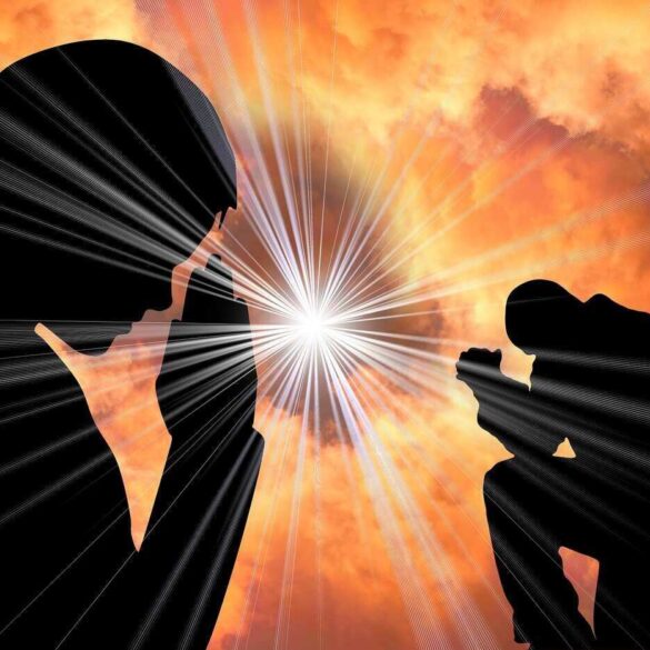 Silhouette of man and woman praying in front of light from sky