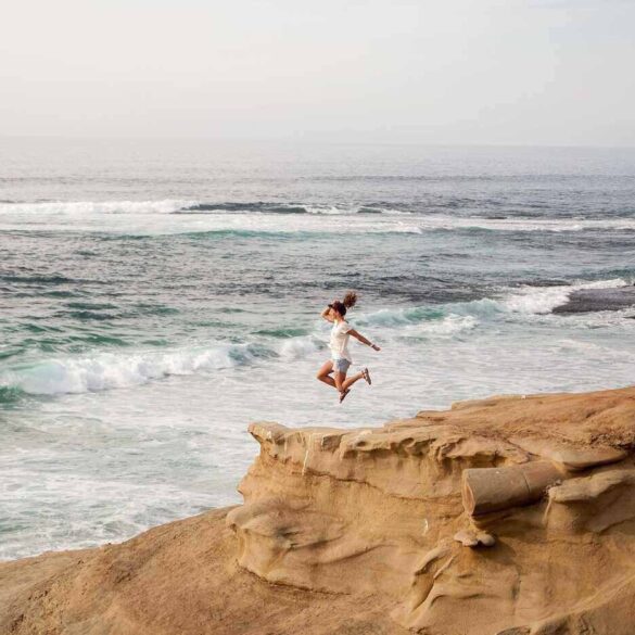 Woman jumping off sand dune into water