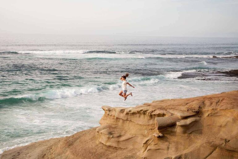 Woman jumping off sand dune into water