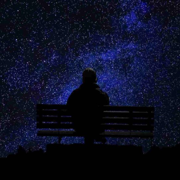 man sitting alone on a park bench looking at the night sky
