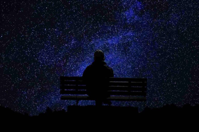 man sitting alone on a park bench looking at the night sky