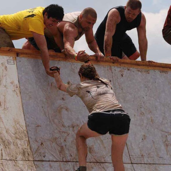 men helping a woman up a steep wall