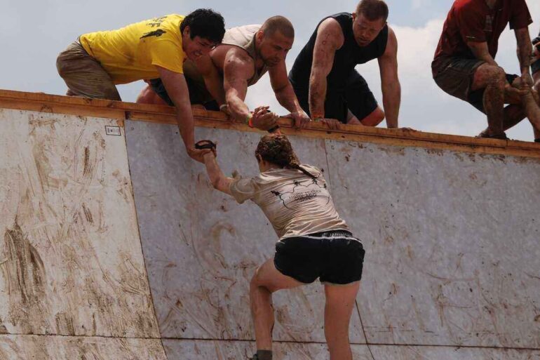 men helping a woman up a steep wall