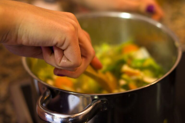 Person stirring vegetables in pot