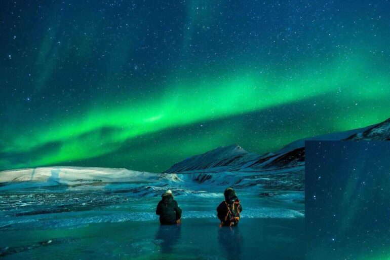 two people in the sea looking at the northern lights