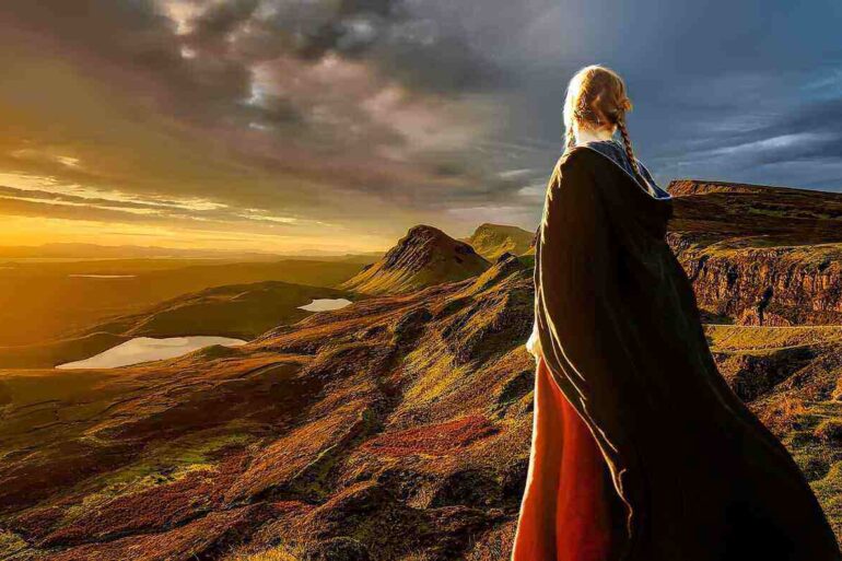 Girl in cape on a mountain watching the sun set