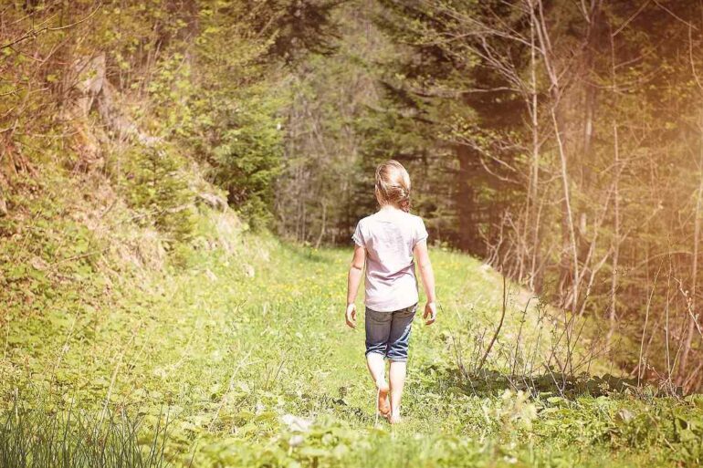 Young girl walking barefoot on grassy path