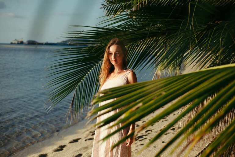 Young woman standing on sandy beach with palm trees - 5 Reflections on Living With Goodness, Exhilaration and More