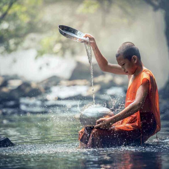 Young boy sitting in a stream, trickling water from a bowl - Spiritual Rituals For Busy People: 9 Mini-Rituals to Do Anywhere