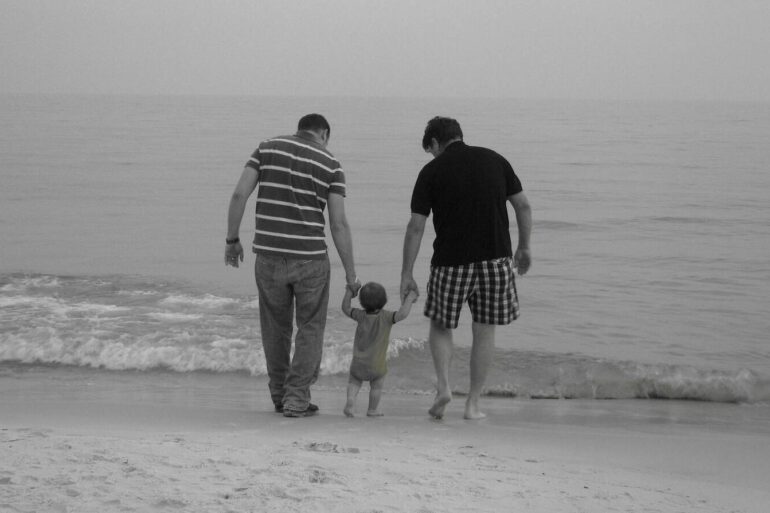 father with adult sun and small grandchild on the edige of a beach