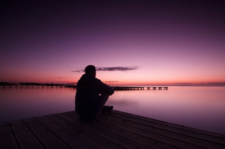 Man sitting on dock beside calm lake - On Retreat With Spiritual Leader Mamo Lorenzo of Sasaima
