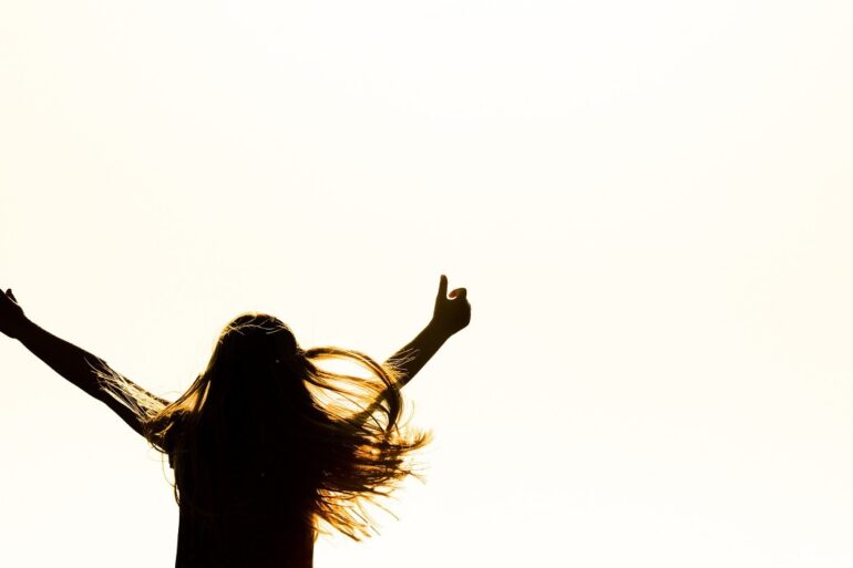 Girl with arms stretched in air in joy - Why Accepting Our Truth Can Lead Us To a Life of Peace
