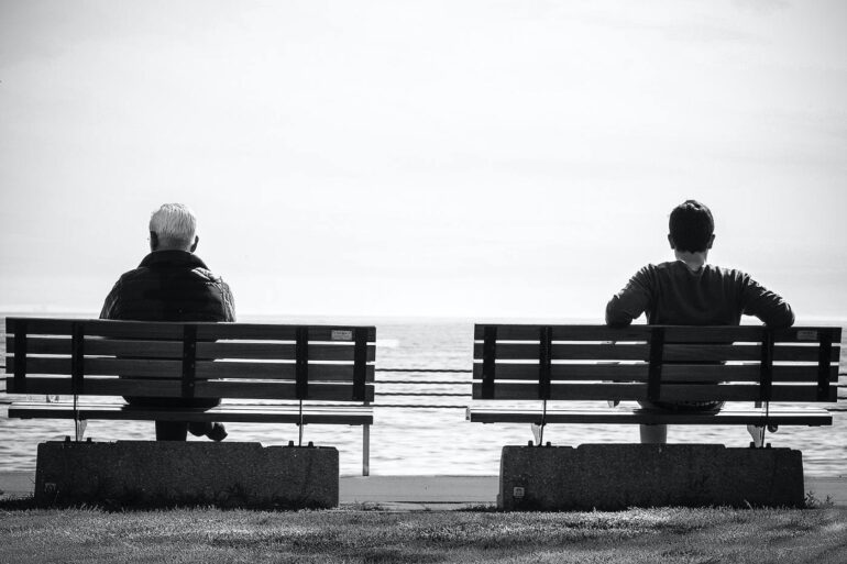 Black and white photo of two men sitting on benches - The Value of Pausing and Reflecting in the Present Moment