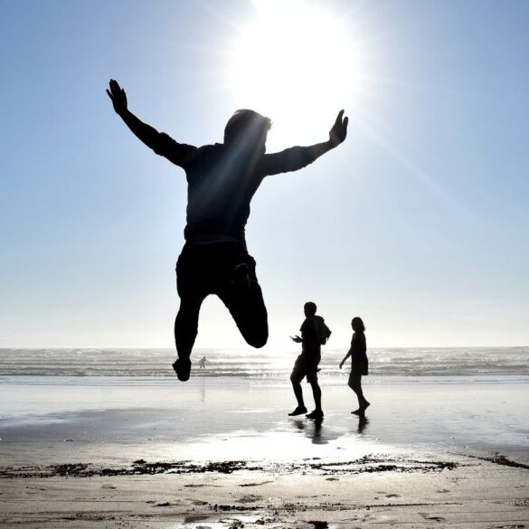 Three silhouettes on sunlit beach, including one of boy jumping - Mindfully Letting the Light of the Sun Drown Out Darkness