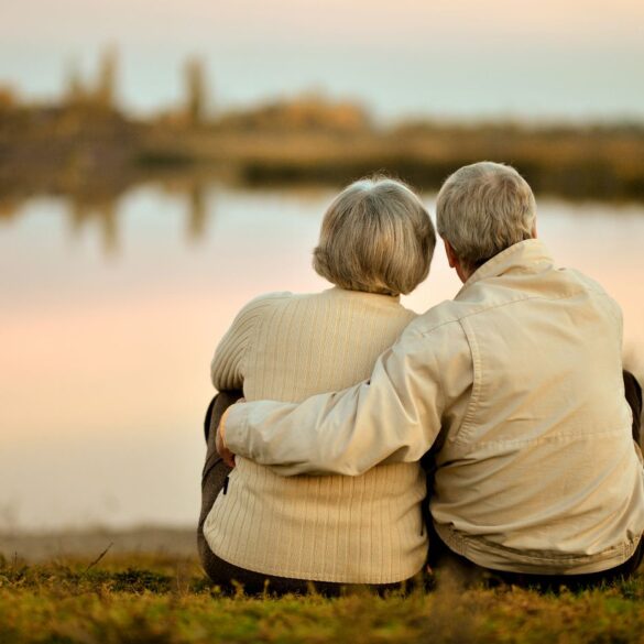 Senior couple with arms around each other, looking at water